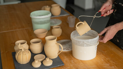 Close-up of a potter's hands glazing a ceramic mug. 