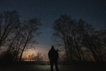 Night scene, silhouette of a man with a rifle behind his back against a background of forest and...