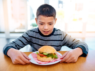 Child, unhealthy and thinking about eating burger at table for fast food, meal and nutrition. Kid,...