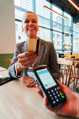 Vertical. Mid adult woman paying the bill with a contactless credit card in a restaurant. Female...