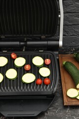 Electric grill with vegetables on black marble table