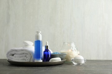 Spa composition. Cosmetic products, terry towel, burning candles and sea salt on gray table against light background, space for text