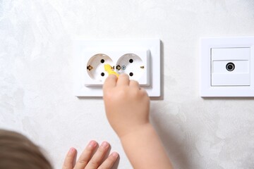 Little child playing with toy screwdriver and electrical socket at home, closeup. Dangerous...