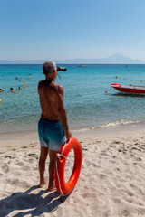The lifeguard looks through binoculars and keeps people safe in the water.