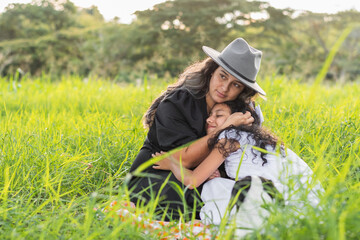 young mother hugging and giving love to her little daughter while sitting on the grass