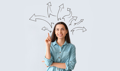 Thoughtful young woman pointing at something on light background