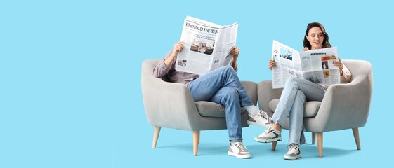 Young couple reading newspapers in armchairs on blue background with space for text