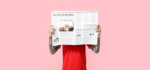 Tattooed man with newspaper on pink background
