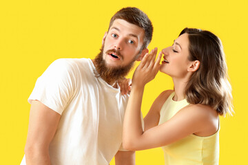 Fototapeta premium Young woman whispering in her boyfriend's ear on yellow background