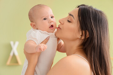 Happy mother kissing her cute little baby in room at home