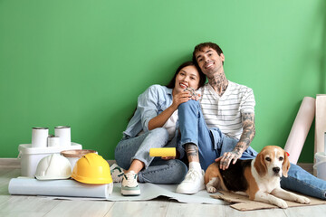 Young couple with painting tools and Beagle dog sitting near green wall during repair in their new...