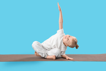 Cute little girl practicing yoga on mat against blue background