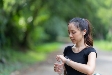 Beautiful young Asian woman in sportswear smiling opens a water bottle to refresh herself before starting a pre-workout preparation. Focus on woman drinking water