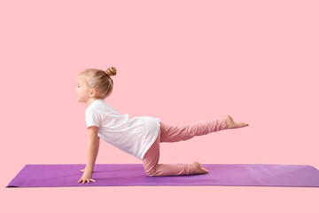 Cute little girl practicing yoga on mat against pink background