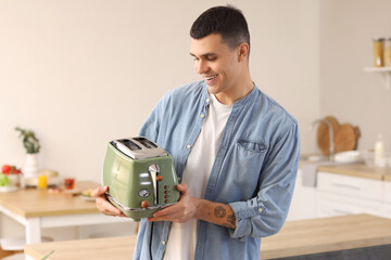 Young man holding modern toaster in kitchen