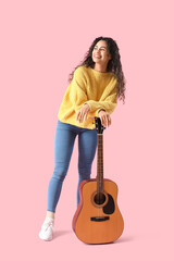 Young African-American woman with acoustic guitar on pink background
