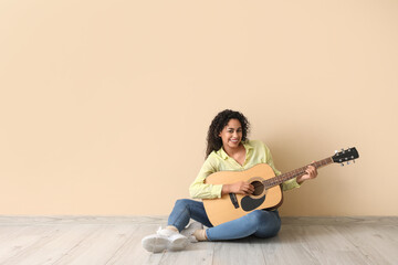 Young African-American woman playing acoustic guitar on beige background