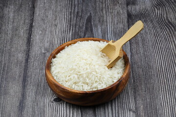 Raw white rice on black background. Long uncooked rice in wooden plate. Natural organic food. Traditional Asian cereal culture.