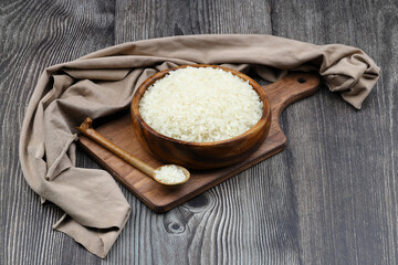 Raw white rice on black background. Long uncooked rice in wooden plate. Natural organic food. Traditional Asian cereal culture.