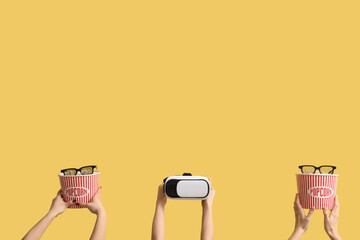 Hands holding buckets with popcorn, VR headset and 3D glasses on yellow background