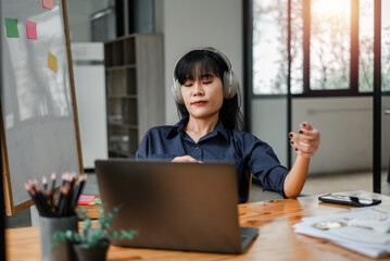 A woman wearing headphones is sitting at a desk with a laptop. She is focused on her work and she is in a serious mood