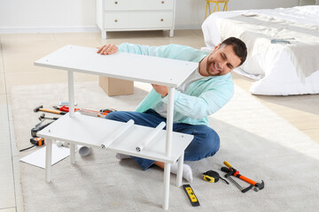 Fototapeta premium Young man assembling white shelf unit in bedroom