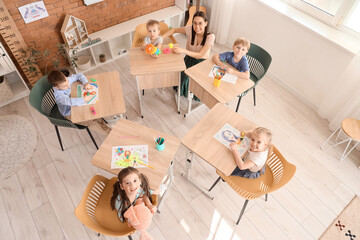 Little children with nursery teacher drawing during art lesson in kindergarten, top view