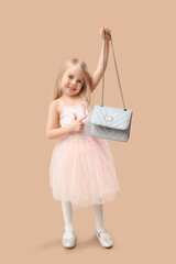 Cute little girl pointing at stylish blue chain bag on brown background