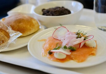 An entree of smoked salmon with herbed cream cheese, red radish, capers, pickled onion, fresh bread rolls, a pat of butter and cookies and cream cheesecake on a business class flight from Sydney to KL
