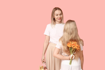 Cute little girl hiding bouquet for mom behind her back on pink background. Mother's Day concept