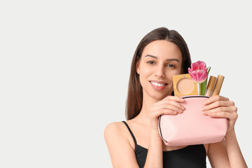 Beautiful young woman holding cosmetic bag with tulip and decorative cosmetics on white background