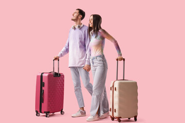 Beautiful young happy couple of tourists with suitcases and headphones on pink background