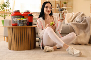 Sporty young woman with protein shake and apple sitting at home