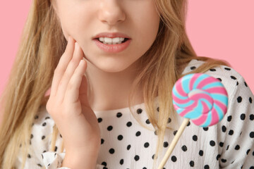 Young girl holding lollipop and suffering from toothache on pink background, closeup