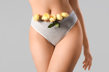 Beautiful young woman in panties with rose flowers on grey background, closeup