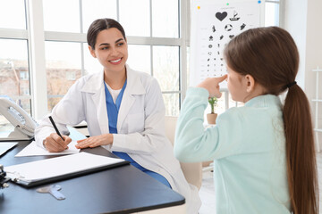 Female ophthalmologist working with little girl at table in clinic