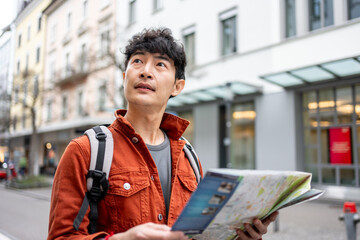 Asian young man backpacker traveler looking at map to find destination. 