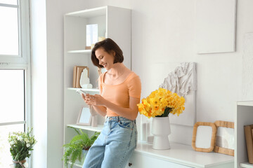 Young woman using mobile phone with daffodils in vase on commode at home