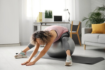 Happy mature sporty woman training with fitness ball at home