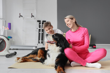 Sporty little boy and his mother with Bernese mountain dog sitting in gym