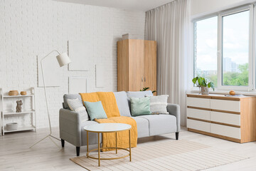 Interior of stylish living room with grey sofa, drawers and closet