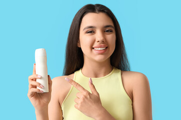 Sporty young woman pointing at deodorant on blue background, closeup