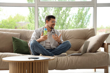 Young man with bottle of cucumber water video chatting on sofa at home