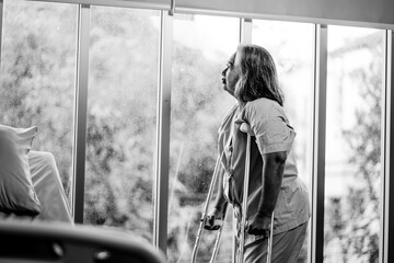 Elderly lady patient using crutches walker looking out glass window. Strong health, medical care...