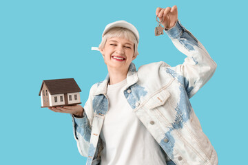 Portrait of beautiful young woman with house model and keys on blue background. Mortgage concept