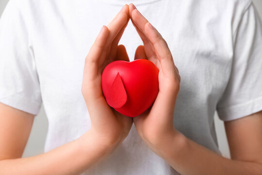 Woman with heart-shaped grip ball and paper blood drop on grey background. World Blood Donor Day