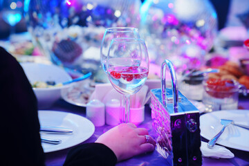 hand with glass on a table set for the holiday in purple in a dark banquet hall.