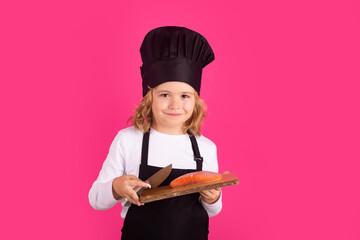 Child cook hold cutting board with fish salmon steak and knife. Cooking, culinary and kids. Little boy in chefs hat and apron on studio isolated background.