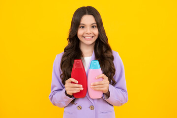 Teenager child girl showing bottle shampoo conditioners or shower gel isolated on yellow background. Hair cosmetic product. Mock up bottle. Happy teenager, smiling emotions of teen girl.