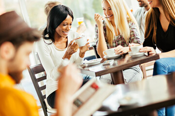 Group of happy diverse women laughing and enjoying coffee together in a cafe
